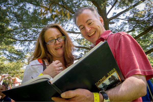 A man and a woman look at a Notre Dame yearbook together, smiling. The cover reads 