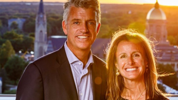 A well-dressed couple posing for a photo with the campus of the University of Notre Dame in the background.